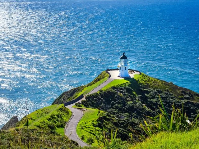Ein Weg, der einen grasbewachsenen Hügel hinunter zum Leuchtturm von Cape Reinga führt.