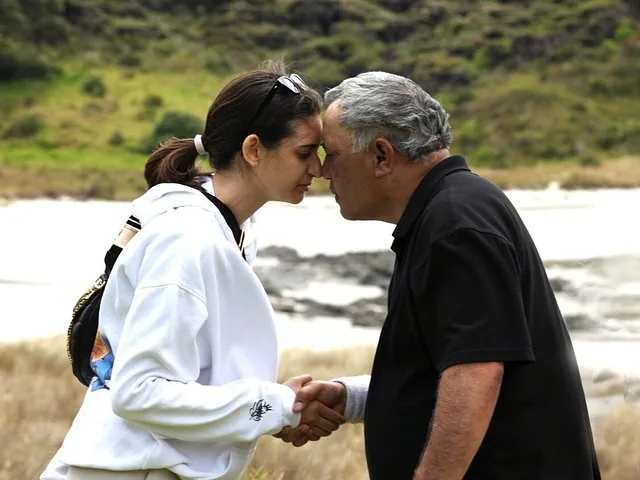 Two people greeting each other with a traditional Maori hongi near a body of water.