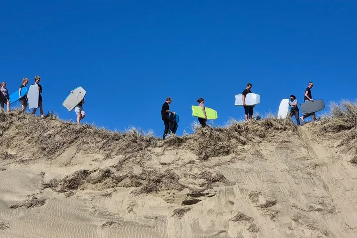 Personen mit Sandboards laufen entlang des Kamms einer großen Sanddüne.
