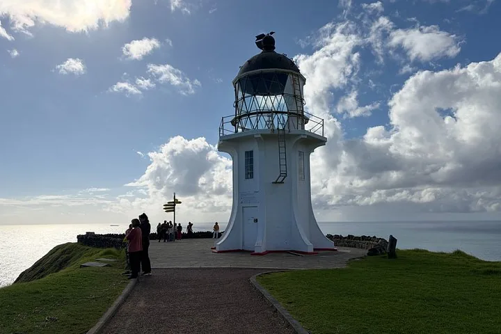 Tourists standing near the Cape Reinga lighthouse under a cloudy sky.