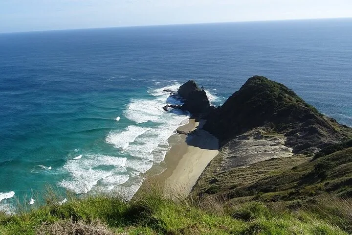 Una vista dalla cima di una scogliera che guarda verso una spiaggia sabbiosa appartata e un promontorio roccioso.