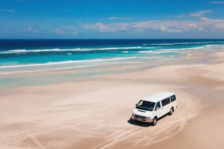 Ein weißer Tourvan parkt am Sandstrand des Ninety Mile Beach.